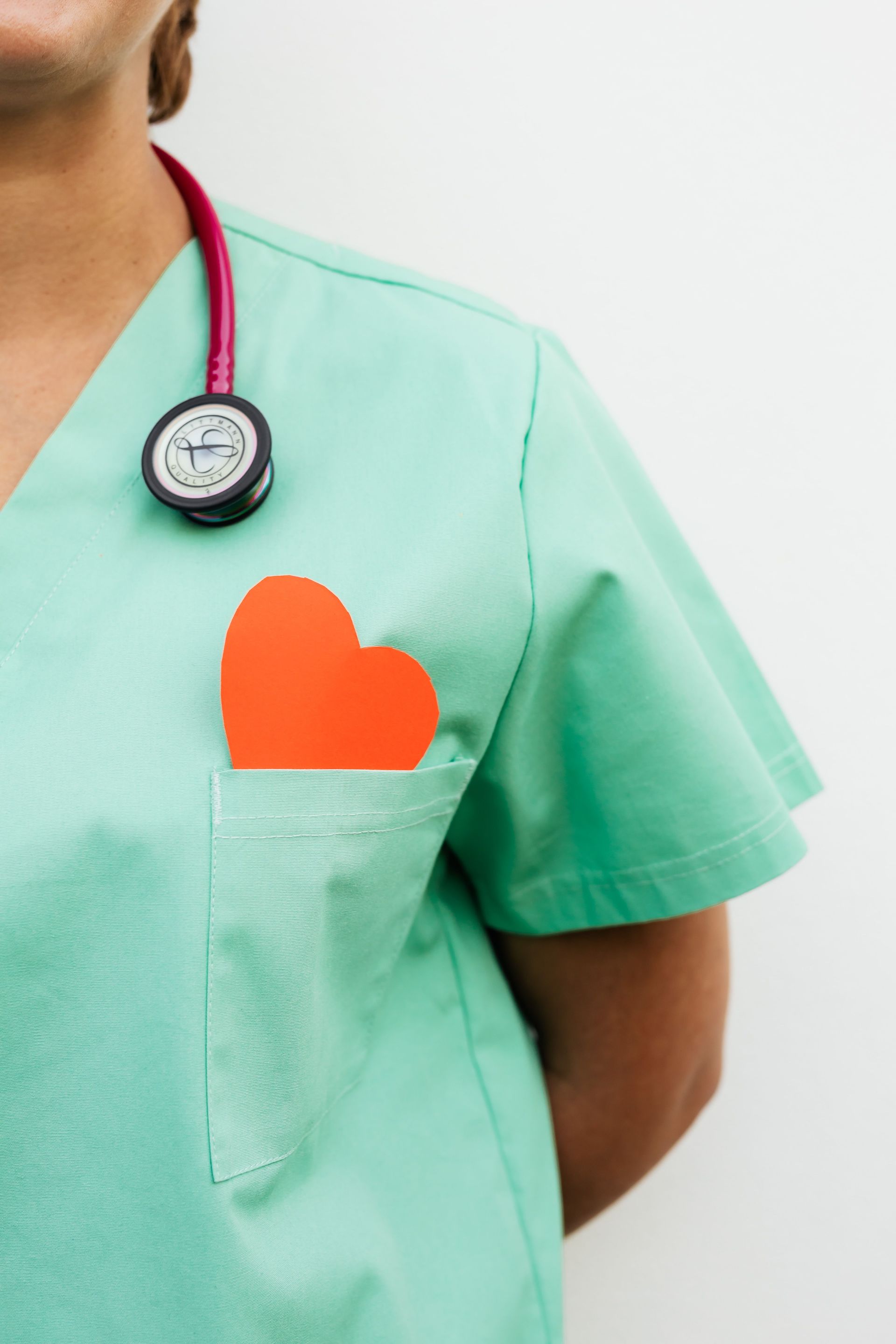Nurse in pastel green scrubs with stethoscope and paper heart for heart health awareness.