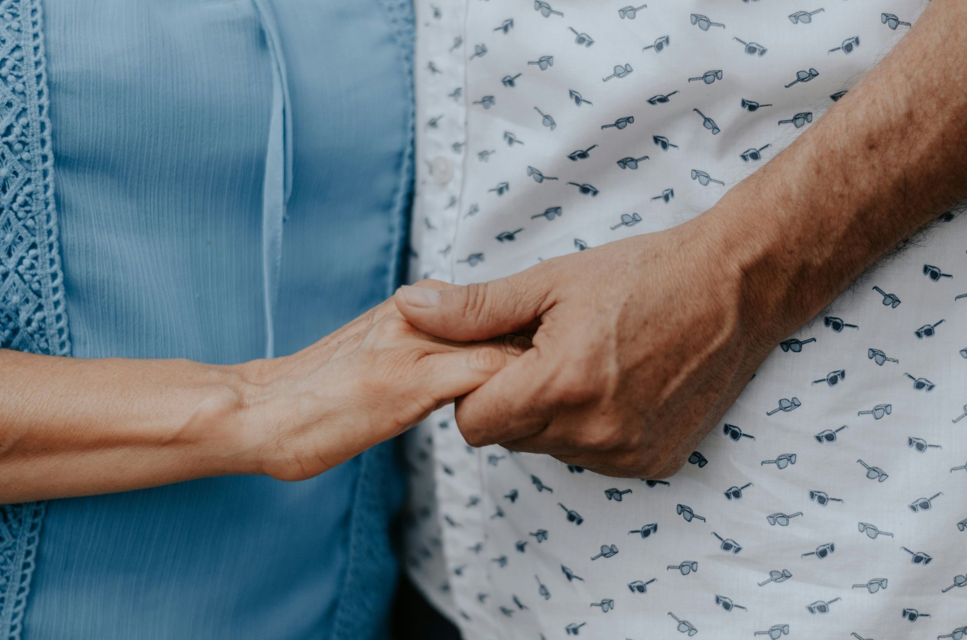 Two people holding hands, one wearing a blue shirt and one a patterned shirt