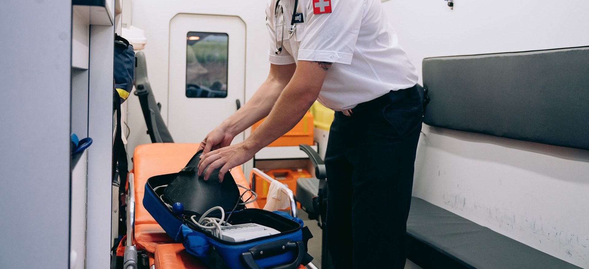 A paramedic organizing medical equipment in an ambulance interior.